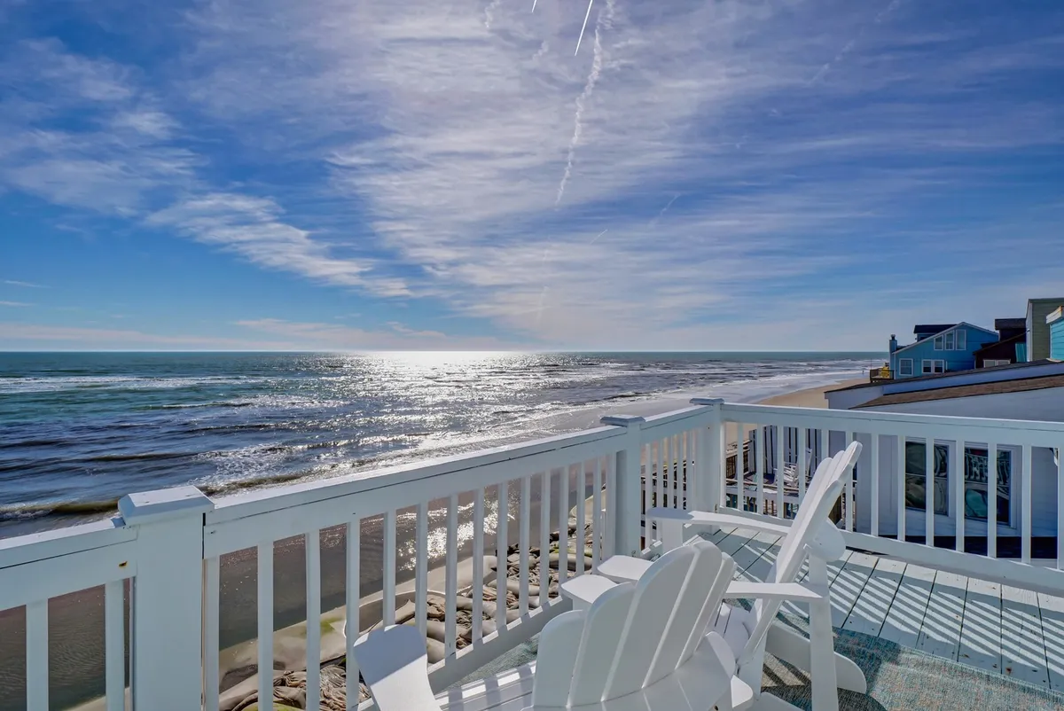 A tranquil view from the private deck overlooking the ocean, with deck chairs facing the bright blue sky and gentle waves. The scene invites relaxation, sunset watching, and family picnics with a stunning backdrop.