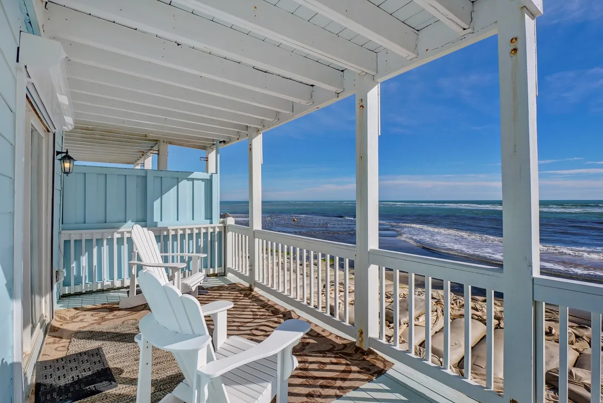 A wooden deck furnished with Adirondack chairs overlooks the ocean, framed by a sturdy railing. The scene is tranquil, inviting occupants to relax with a book, soak in the sea breeze, or watch sunsets. The deck’s design suggests easy access from inside, ideal for both people and pets to lounge or head straight out for beach walks.