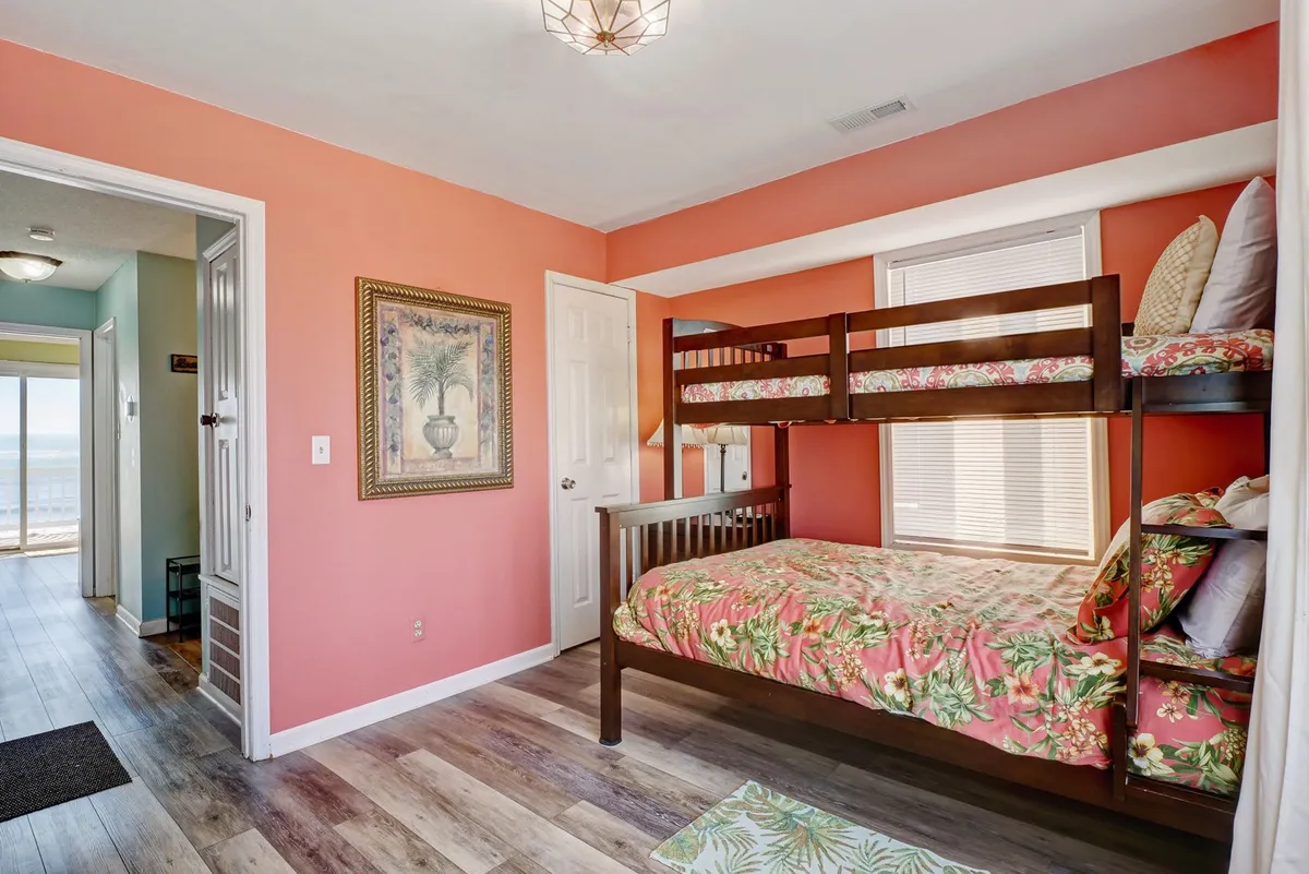 A playful bunk room with a twin-over-full bunk bed adorned in floral bedding, colorful wall paint, and decorative wall art. The room feels lively and welcoming, perfect for children or friends sharing a fun sleepover by the sea.