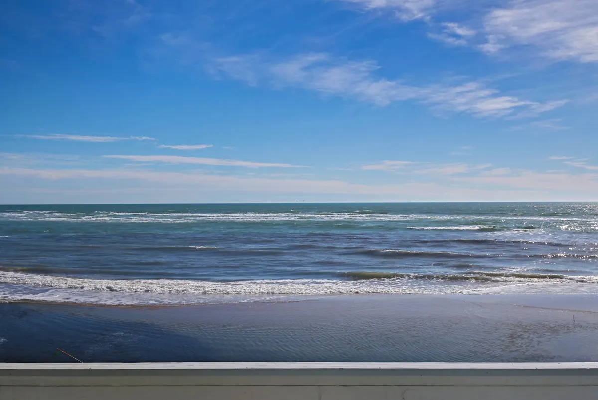 A sweeping view of the ocean with gentle waves rolling toward the shore, under a clear horizon line and expansive sky. The natural beauty and tranquility of the seascape are central, evoking a sense of serenity and a deep connection to the ocean.