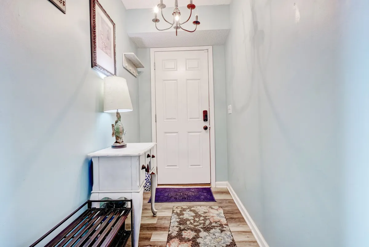 A welcoming interior entryway featuring a front door, lamp, console table, and rug. The space is inviting and hints at the comfort awaiting inside, suggesting the beginning of a gathering as guests arrive.
