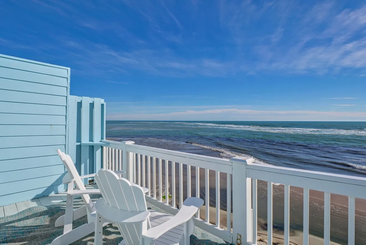 A pair of Adirondack chairs positioned on a deck overlooking the vast ocean and a clear blue sky. The view is open and unobstructed, perfect for sunrises, stargazing, or quiet contemplation with the sea as your backdrop.